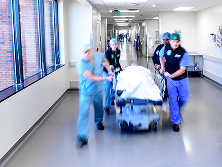 Various emergency medical personnel are transporting a trauma patient on a gurney in a hospital hallway, 2019.