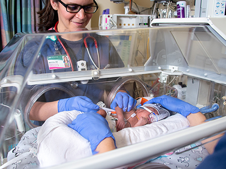 Nurse wearing blue safety gloves is tending to a premature baby in a neonatal incubator in the Regional Neonatal Intensive Care Unit (NICU), 2019.