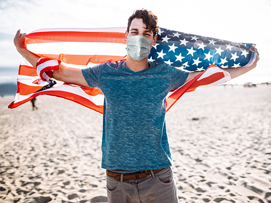 Masked person holding American flag over head. 