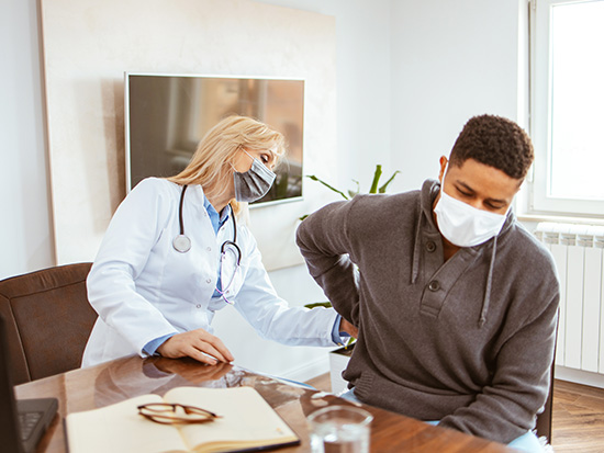 Young African-American man being examined by female doctor in a doctor's office. Man with protective face mask complained of kidney pain.