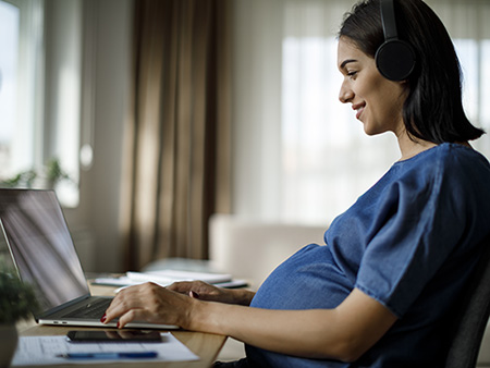 Pregnant woman with headphones using laptop