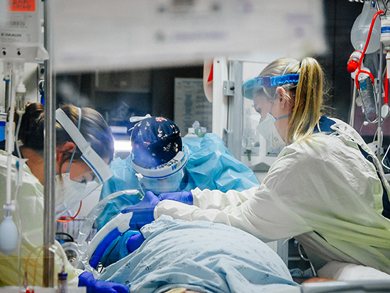 Grace Marett, RN (Registered Nurse, Medical Nursing), Shelby Roberts, RN (Registered Nurse, Medical Nursing), and Meghan Kelly (Certified Respiratory Therapist, Respiratory Care) are wearing PPE (Personal Protective Equipment) face shields, face masks, and gowns while tending to a COVID-19 patient being treated at UAB Hospital for COVID-19 (Coronavirus Disease), December 2020. 