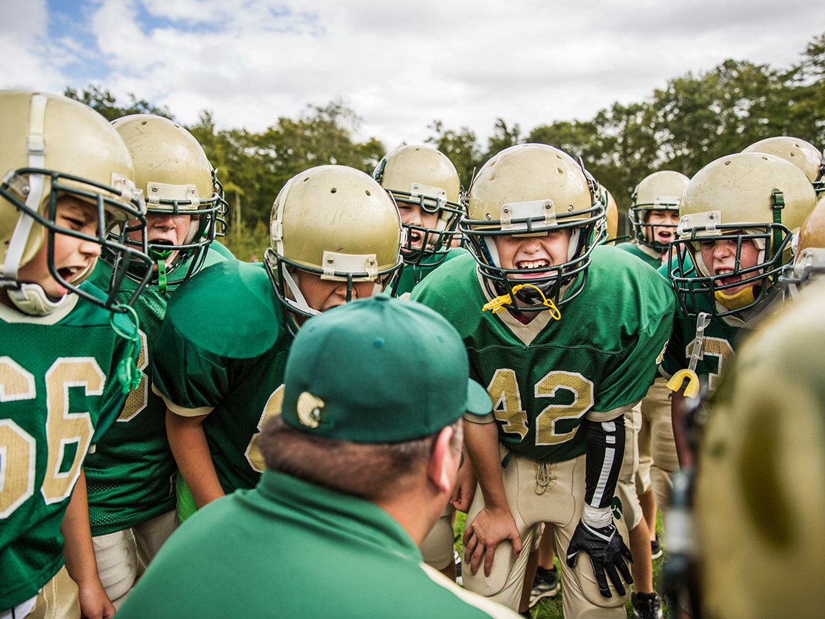 Young football players stand on the sideline.