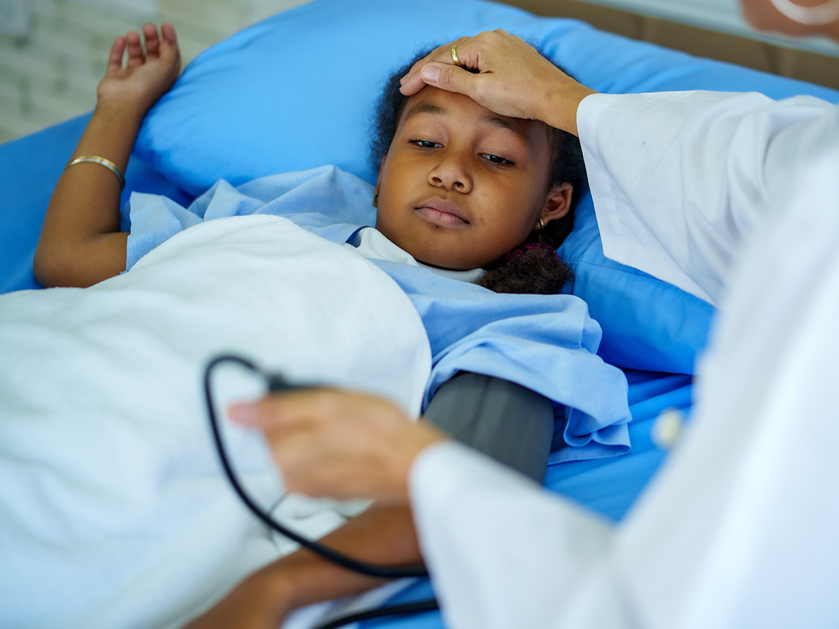 Child lays on blue medical bed while blood pressure is being taken by doctor