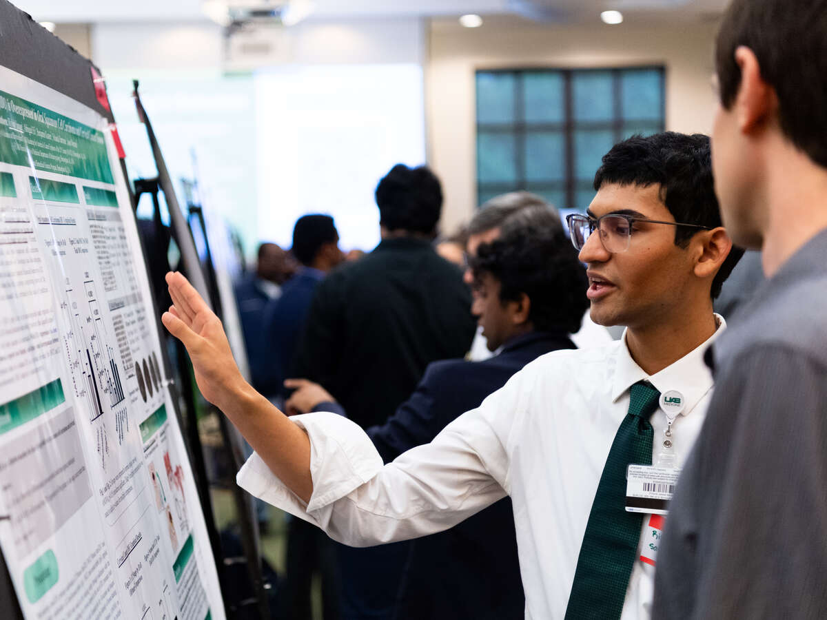 UAB Expo In-Person Poster Presentation in Alumni House, Summer 2024 - Service Learning and Undergraduate Research. Unknown male student is discussing his presentation with an unknown male, July 2024.