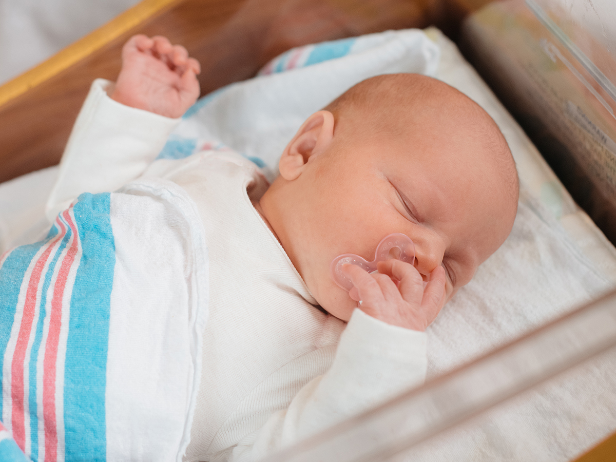 Close-up of newborn baby lying in hospital baby crib.