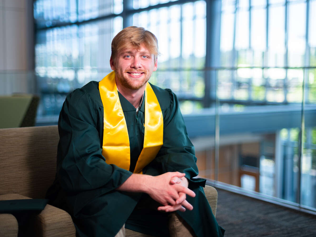 Male student wearing commencement cap and gown, sitting in the hall at the UAB Collat School of Business