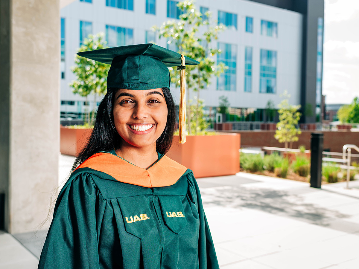  Outdoor photo of Ann Varghese in green commencement regalia.