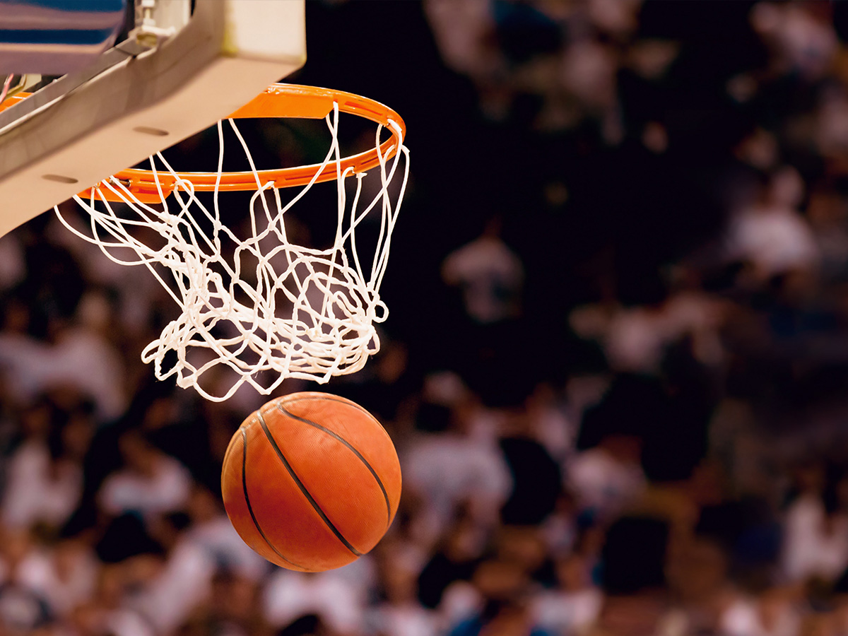 Stock image of a basketball going through a basketball hoop in an arena setting. 