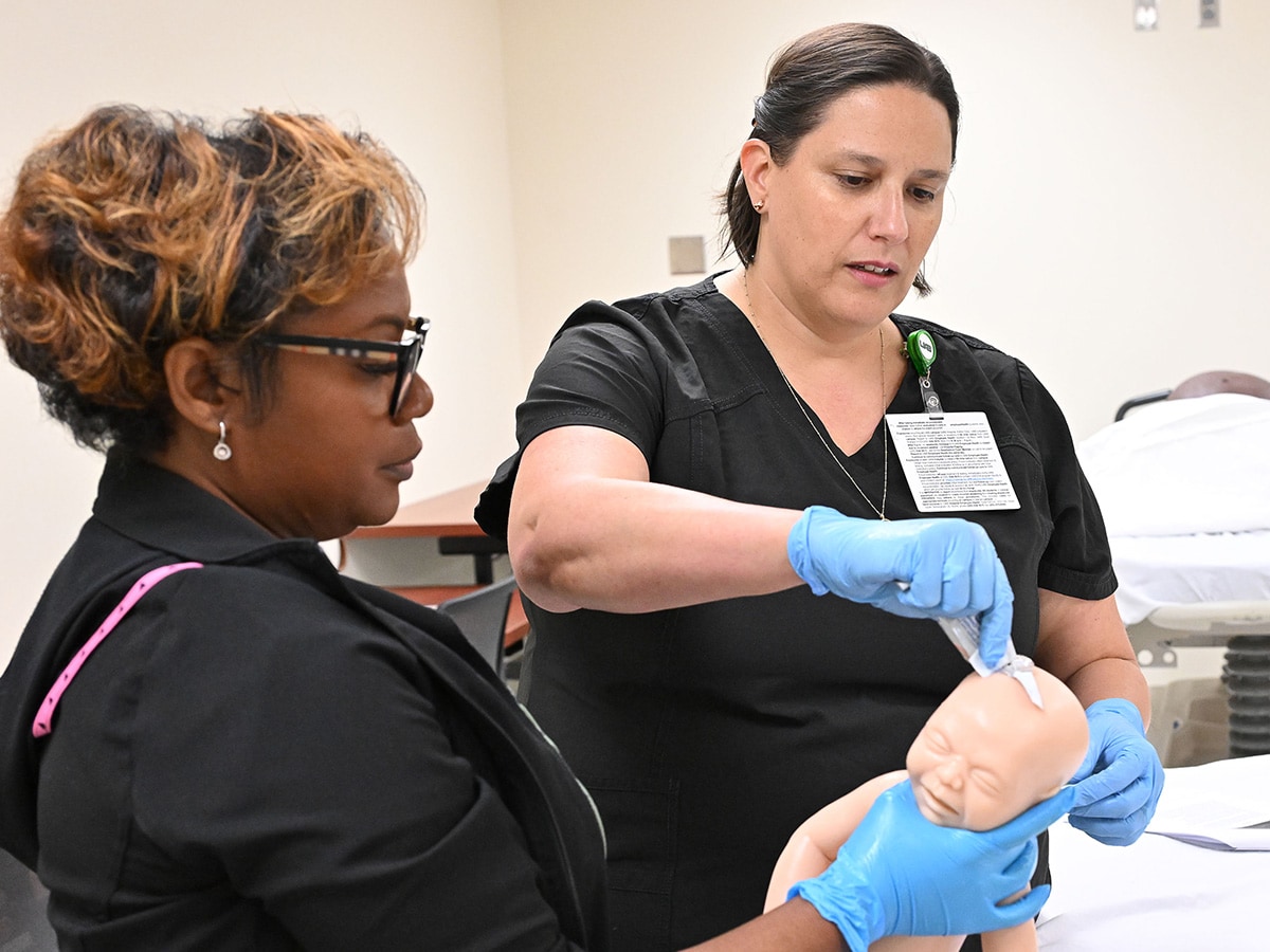 Two nurses practicing care on a simulation baby doll.