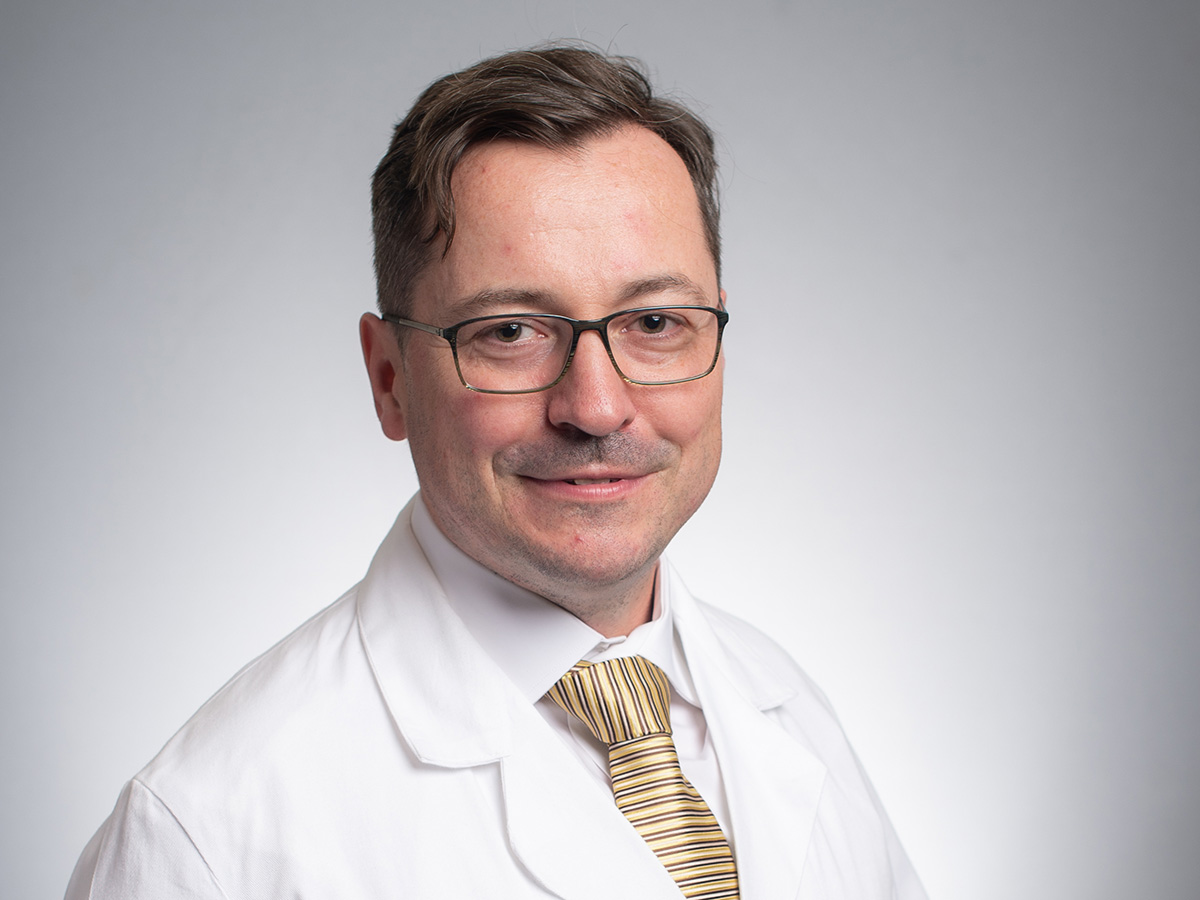 Rafael Grytz headshot on grey background with yellow striped tie.