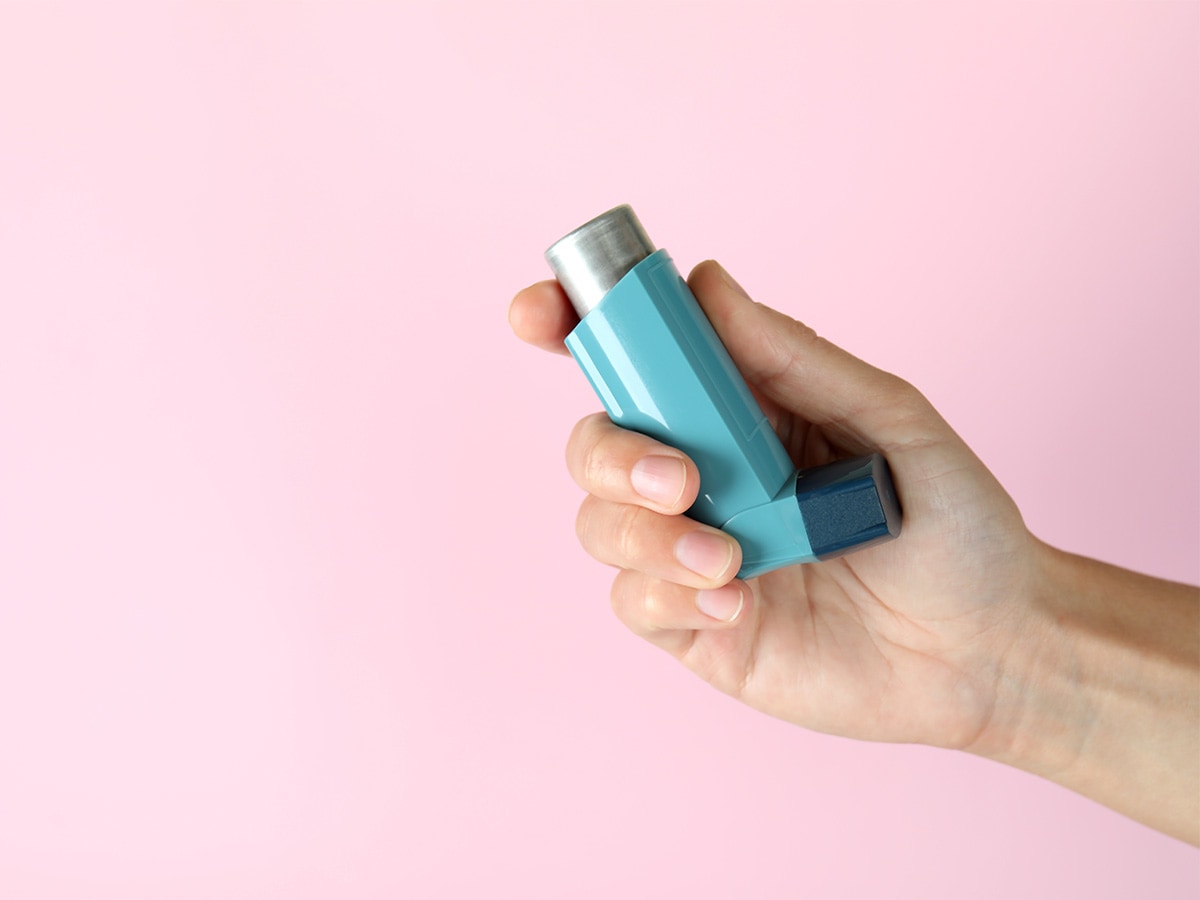 hand holding a blue inhaler with a pink background.