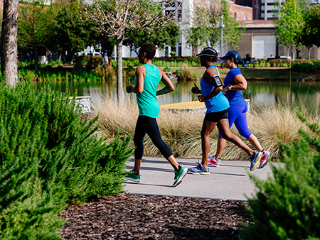 From side, three black women are jogging on paved trail in Railroad Park, 2019