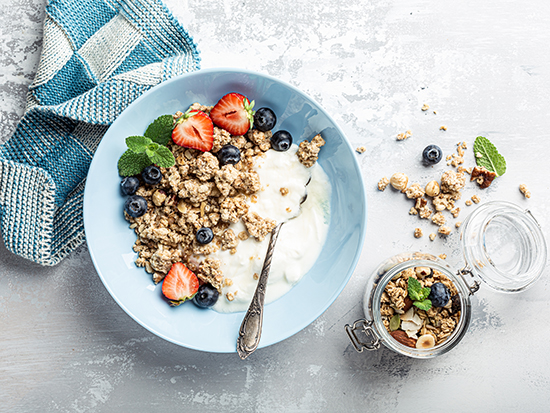 Overhead schoot of granola with nuts mix, yogurt, fresh berries and honey on blue plate voor healthy breakfast