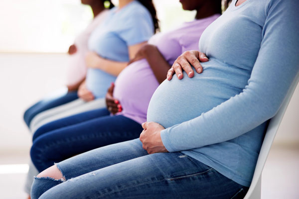 Pregnant women sitting in a waiting room while touching their stomach.