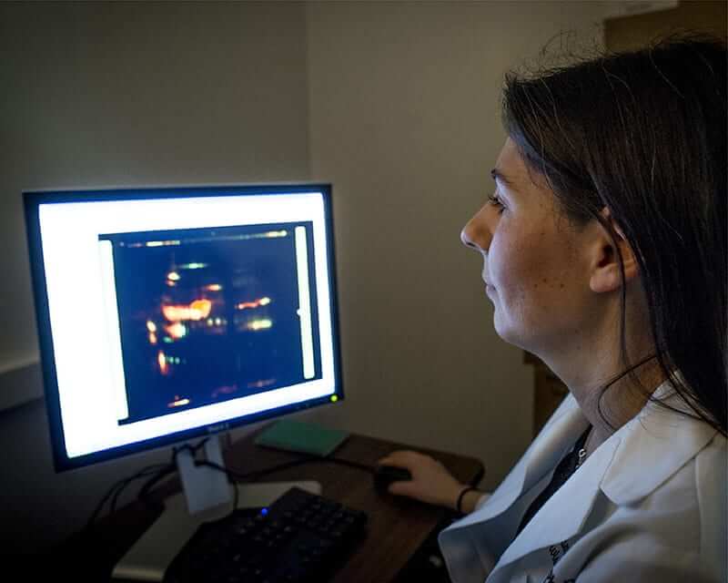 Woman in a lab coat looking at results on a computer screen. 