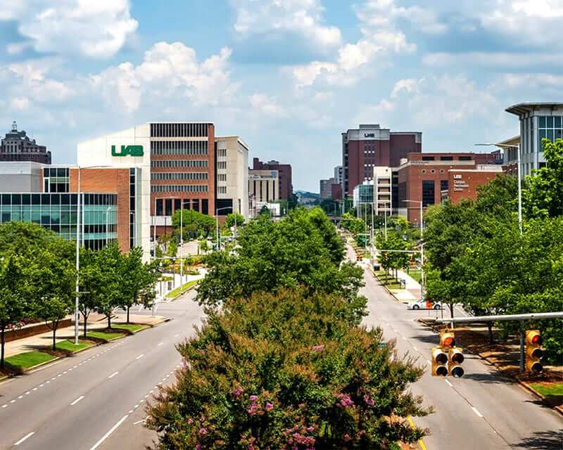 University Boulevard with a median of leafy green trees, lined by UAB campus buildings.