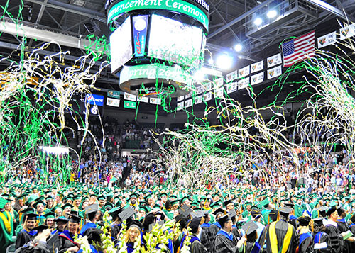 A large crowd of UAB graduates in graduation attire standing at commencement with confetti above their heads.