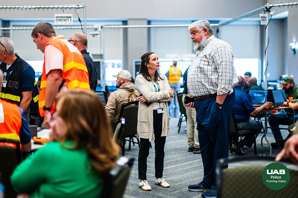 Two participants talk in the center of the frame while dozens of participants gather in small groups or at computers behind them
