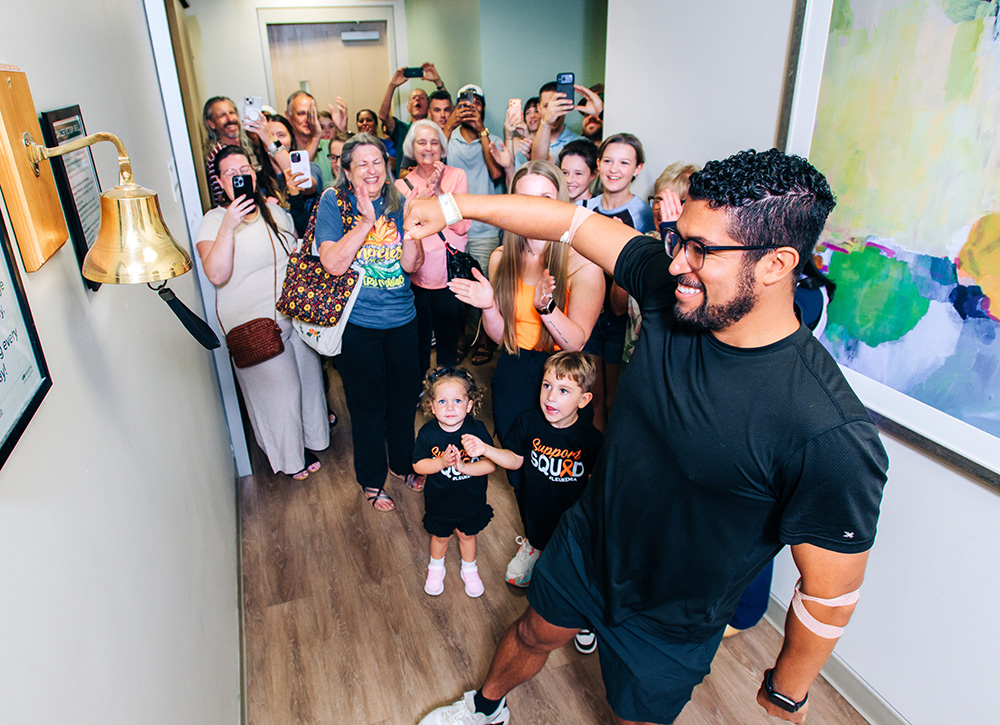 A young man rings the bell at UAB's Kirklin Clinic with family and friends cheering in the background