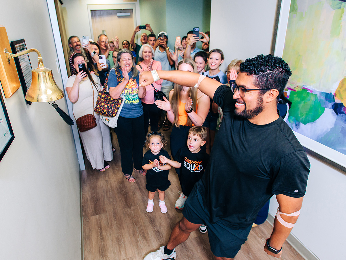 A young man rings the bell at UAB's Kirklin Clinic with family and friends cheering in the background
