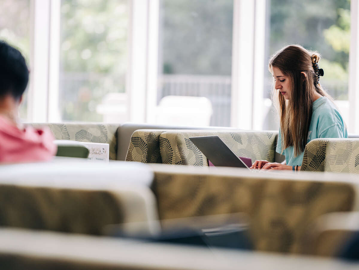 A UAB student typing on her laptop while seated near a window.