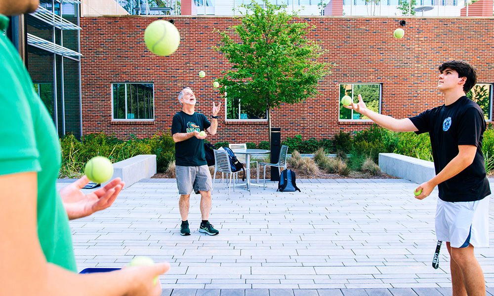 A group of students and faculty juggle tennis balls outside Gorrie Hall