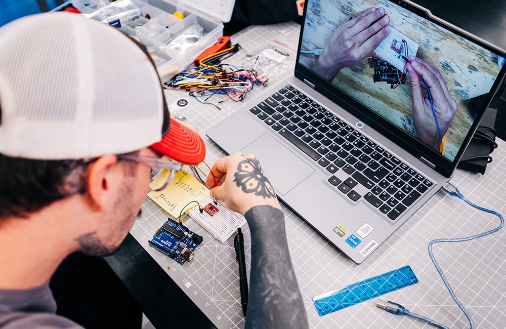 Riggins plugs circuits into a breadboard as he watches a YouTube tutorial on his laptop