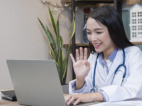 An asian doctor waves while video chatting with colleague.
