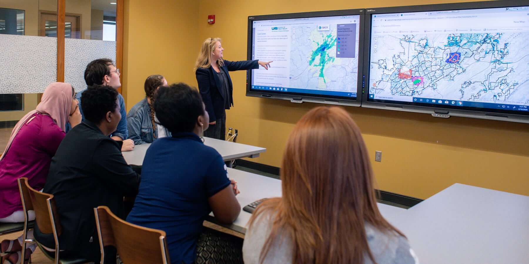 Female professor teaching students using tv displays to present class material.