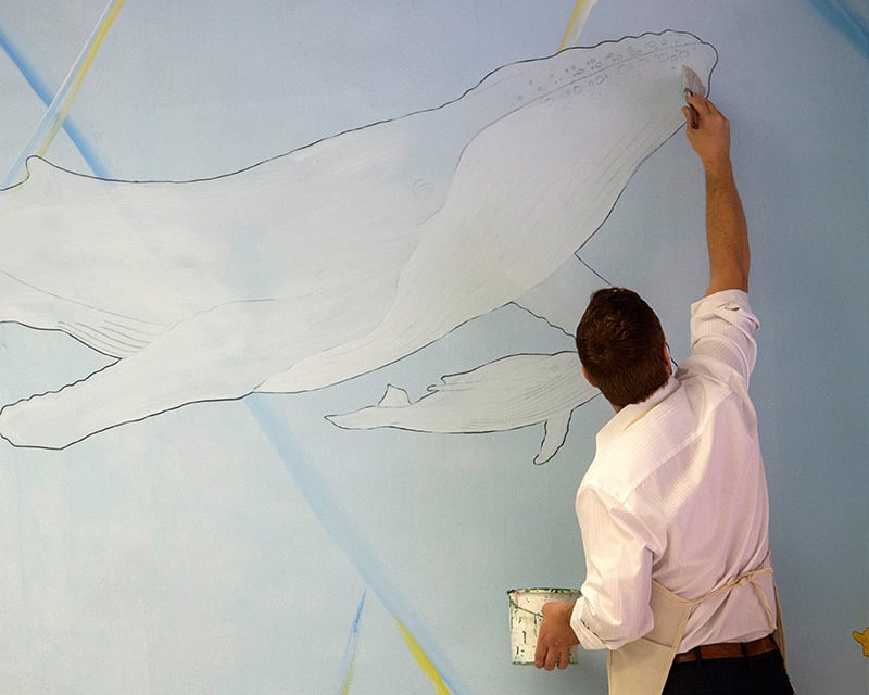 Man painting a mural featuring a swimming whale.