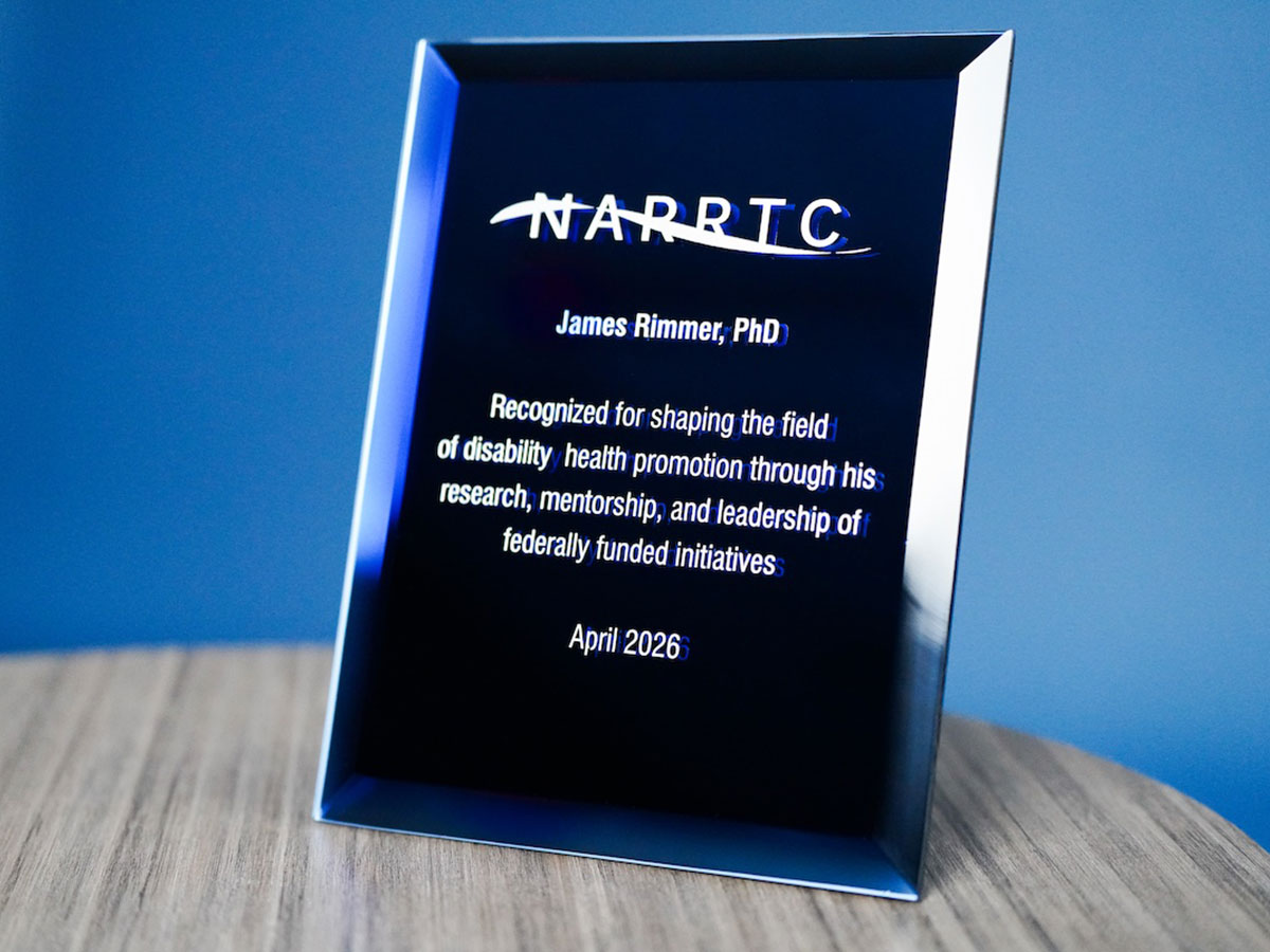 A black, glassy award plaque from the NARRTC to Rimmer sits on a light wood table in front of a blue wall.