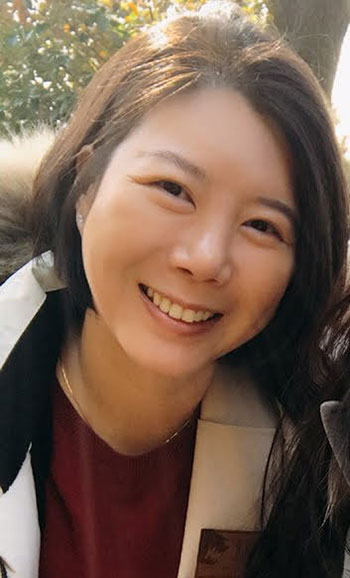  Dr. Kim has short dark hair. She's wearing a winder coat and a dark red shirt. A thin gold chain peaks out over the shirt's collar. 