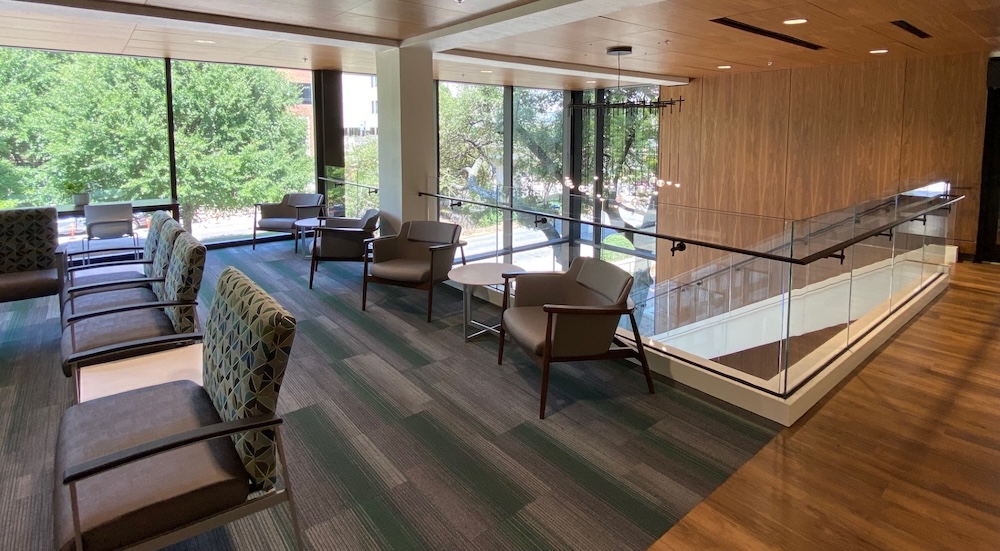 Looking toward the floor to ceiling windows you see comfortable chairs, carpeted floor, and the open stairwell that leads to the first floor.