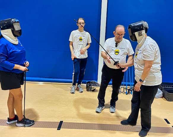 Coach Murray explains a detail to Pound while the assistant coach and a BVI fencer look on.