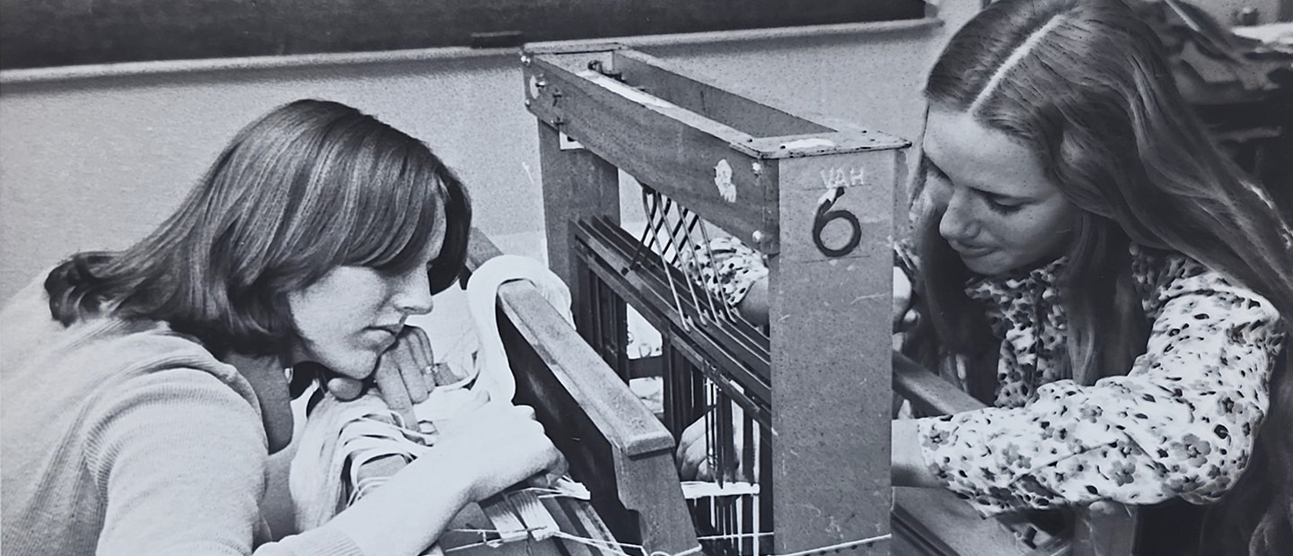 Two young women working on what appears to be a small loom in the 1970s. Picture is black and white.