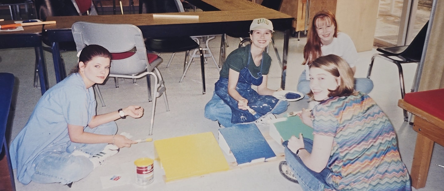 4 young women sit on the floor painting posters.