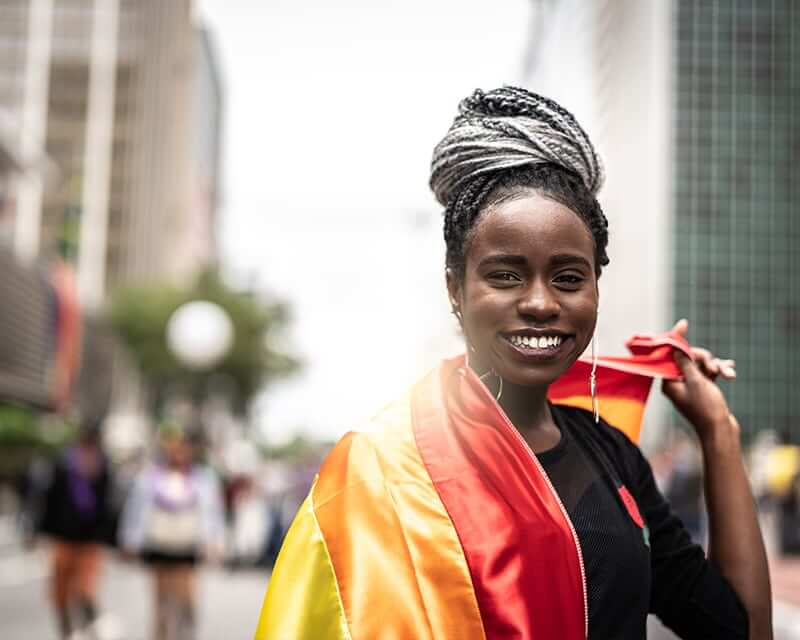 A black woman with a Pride flag wrapped around her shoulders.