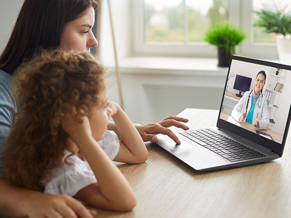 A woman and child talking to a doctor over video call on a laptop. 
