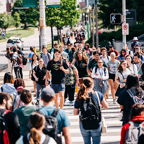 Large crowd of students, most wearing backpacks, are walking in crosswalk on University Boulevard, September 2022.