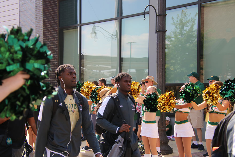 Two football players march by surrounded by UAB Cheerleaders during The Blazer Walk into Protective Stadium for Family Weekend 2021