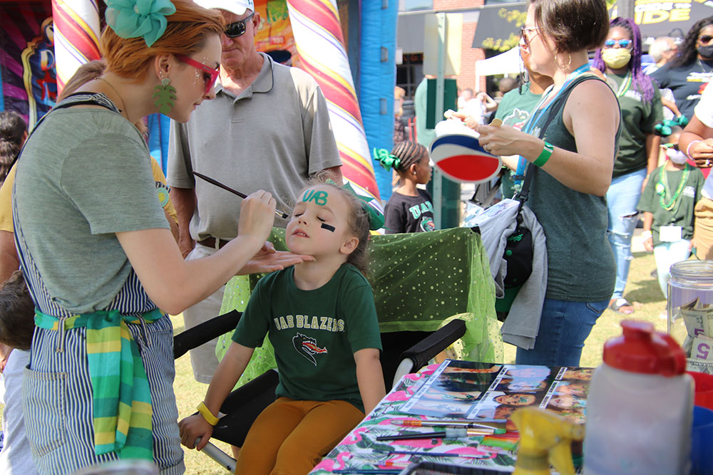 A child getting "UAB" painted across her forehead by a Family Weekend 2021 volunteer