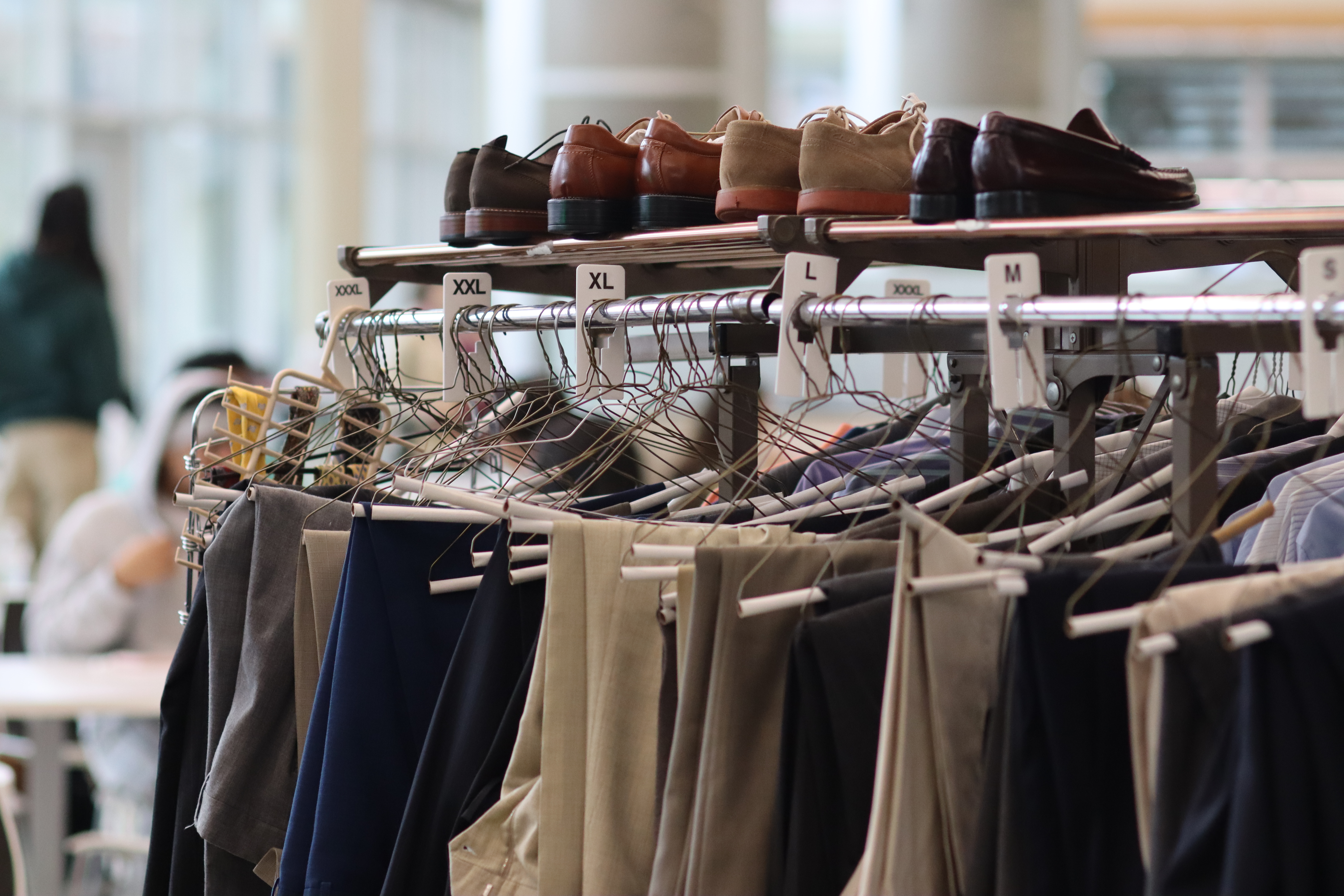 A rack of donated professional slacks organized by size, with dress shoes displayed on the shelf above.