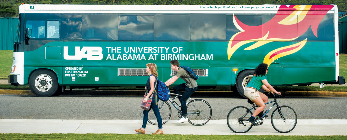 Image of a UAB bus in the background with two bike riders and a pedestrian on the sidewalk.