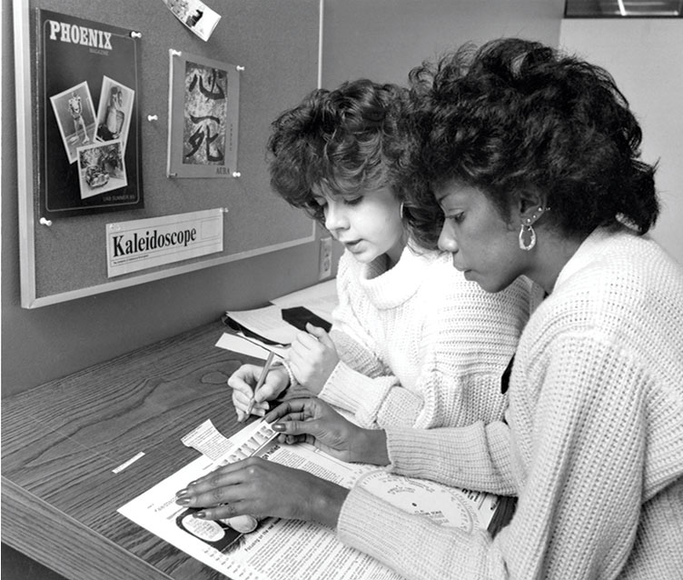 Photo two 1986 staff members piecing together page layout