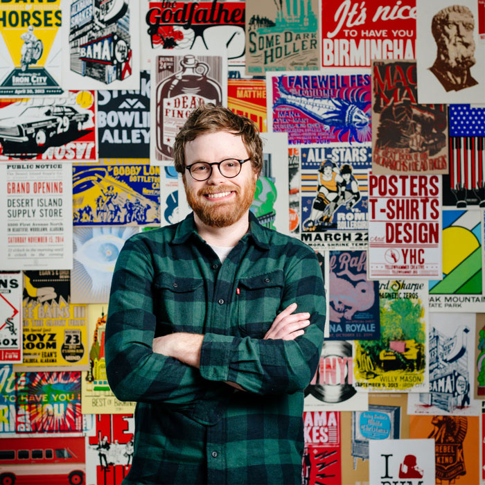 Photo of Brett Forsyth in front of wall of printed layered Yellowhammer Creative posters