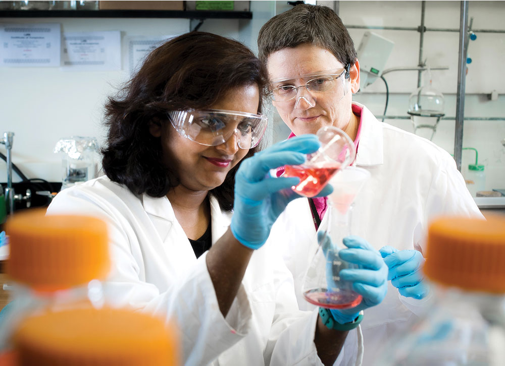 Photo of Nirzari Gupta and Veronika Kozlovskaya in lab pouring red solution into vessel