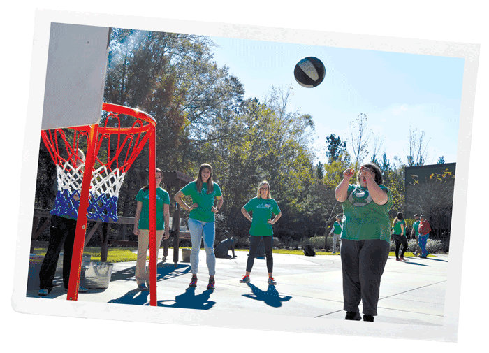 Students help a participant throw a basketball toward a hoop