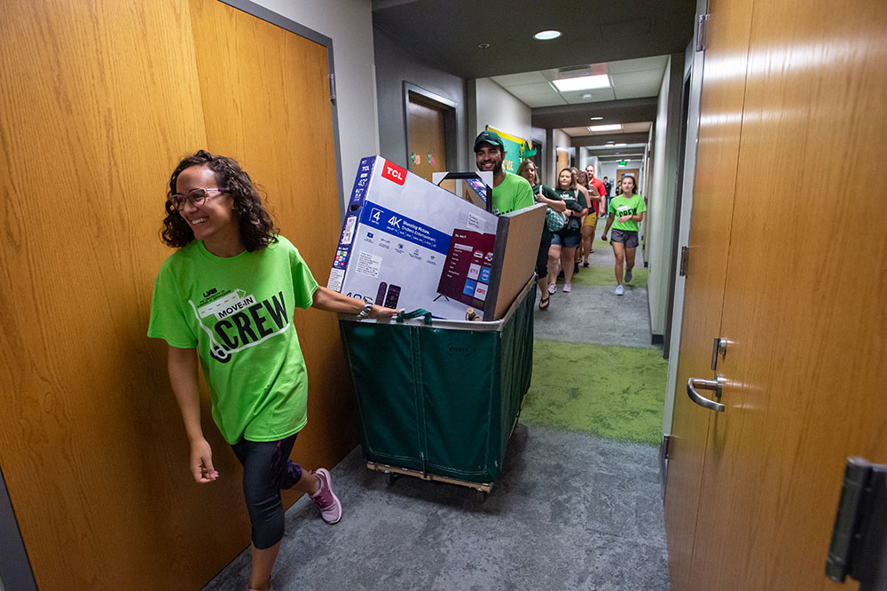 Photo of volunteers moving student belongings in cart inside residence hall
