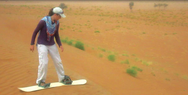 Photo of Rebecca Hyde sandboarding down a dune